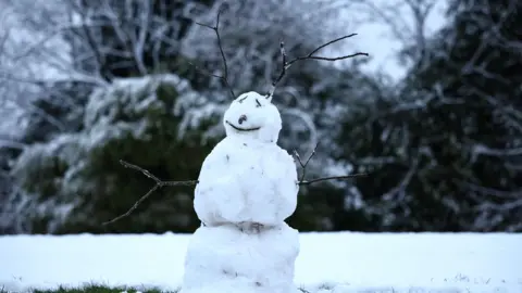 A snowman stands amidst snow at Sefton Park in Liverpool, with branches coming out of its head like antlers.