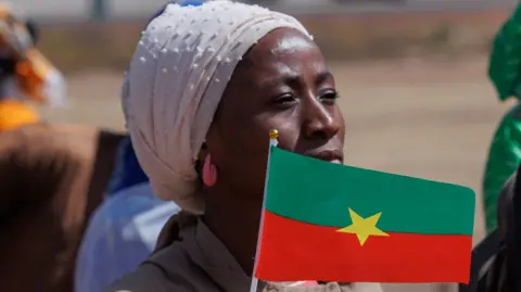 A woman wearing headscarf and pink earrings waves the flag of Burkina Faso