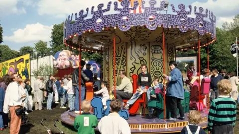 Children and adults pile onto Keith Haringu2019s carousel in Hamburg as others watch on.