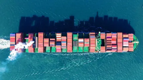 This aerial picture shows a container ship carrying containers of various colours sailing out of Qingdao port, in China's eastern Shandong province. All around it are blue waters reflecting the shadows of the containers.     