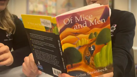 Two pupils in school uniform looking at a copy of the novel Of Mice and Men