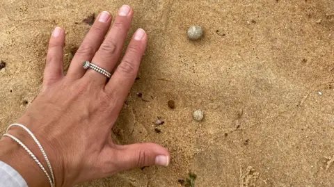 Two small grey balls in sand with a hand for size reference