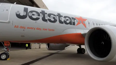 A Jetstar plane sits on the tarmac at an airport in Melbourne, near a hangar.