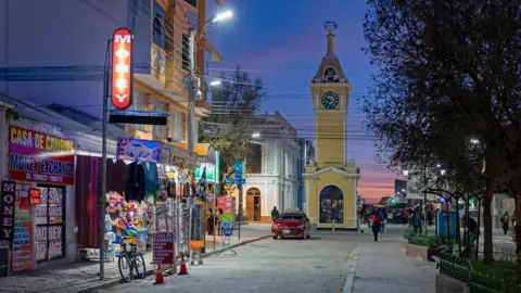 A file photo of shops in the main street and yellow clock tower in the city Uyuni after sunset.