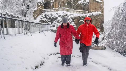 People dressed in red coats walk in snowy conditions at Knaresborough Castle in Knaresborough, Yorkshire.