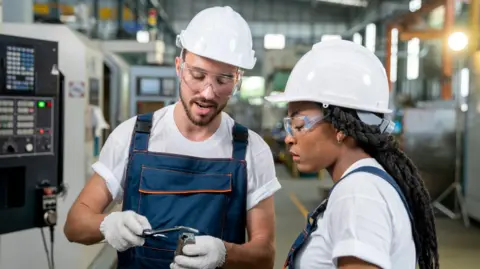 Two engineers wearing white hard hats looking at a piece of equipment