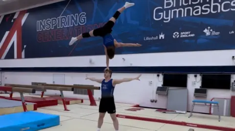 Splitz Gymnastics Club Archie standing in a star shape with Samuel balancing on his head with one hand, also in a star shape