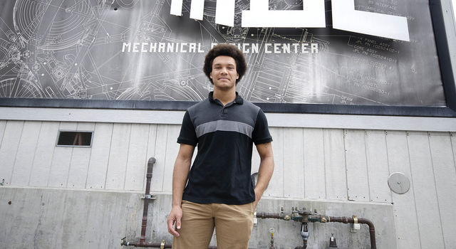 Brandon Ethridge stands in front of a mural made to look like a blueprint on the Mechanical Design Building at JPL.