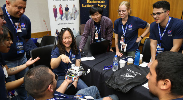 Amiee Quon points to a small rover built out of legos as her team stands in a circle around her examining the rover.