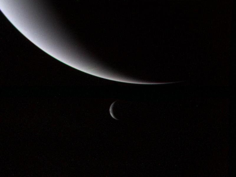 This dramatic view of the crescents of Neptune and Triton was acquired by Voyager 2 approximately 3 days, 6 and one-half hours after its closest approach to Neptune north is to the right.