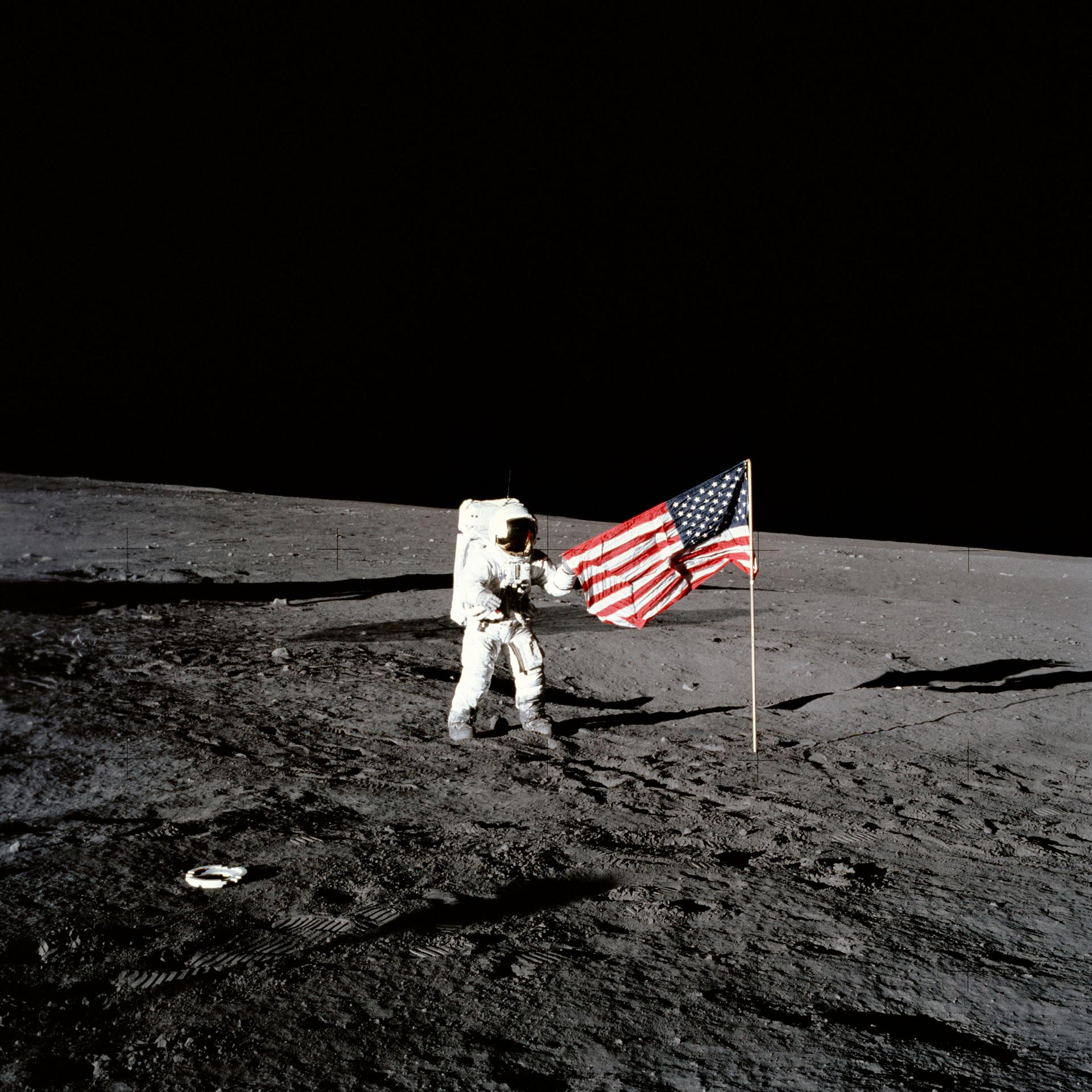 Apollo 12 astronaut stands beside United States flag 