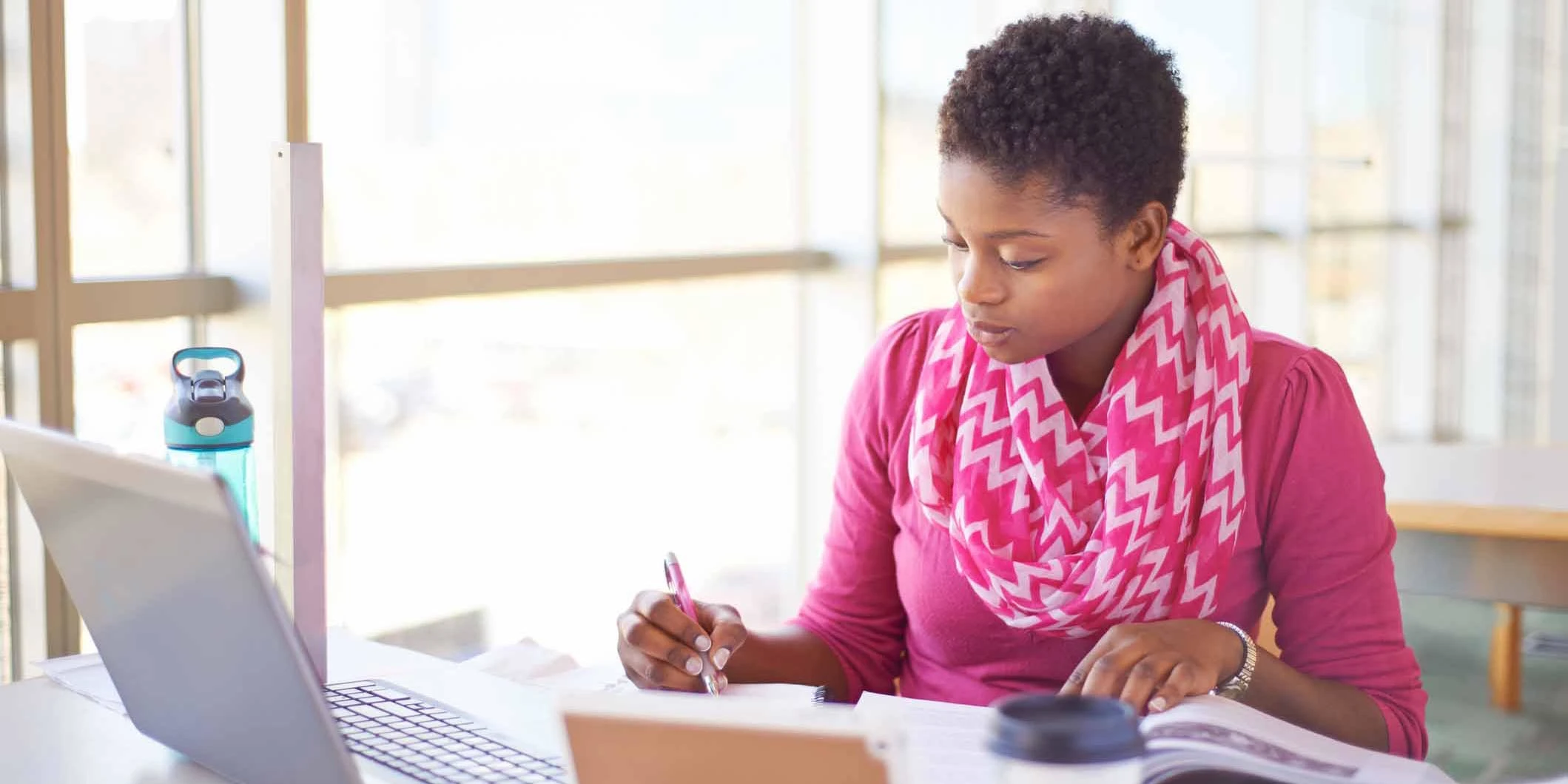 Researcher with laptop at desk and writing on pad