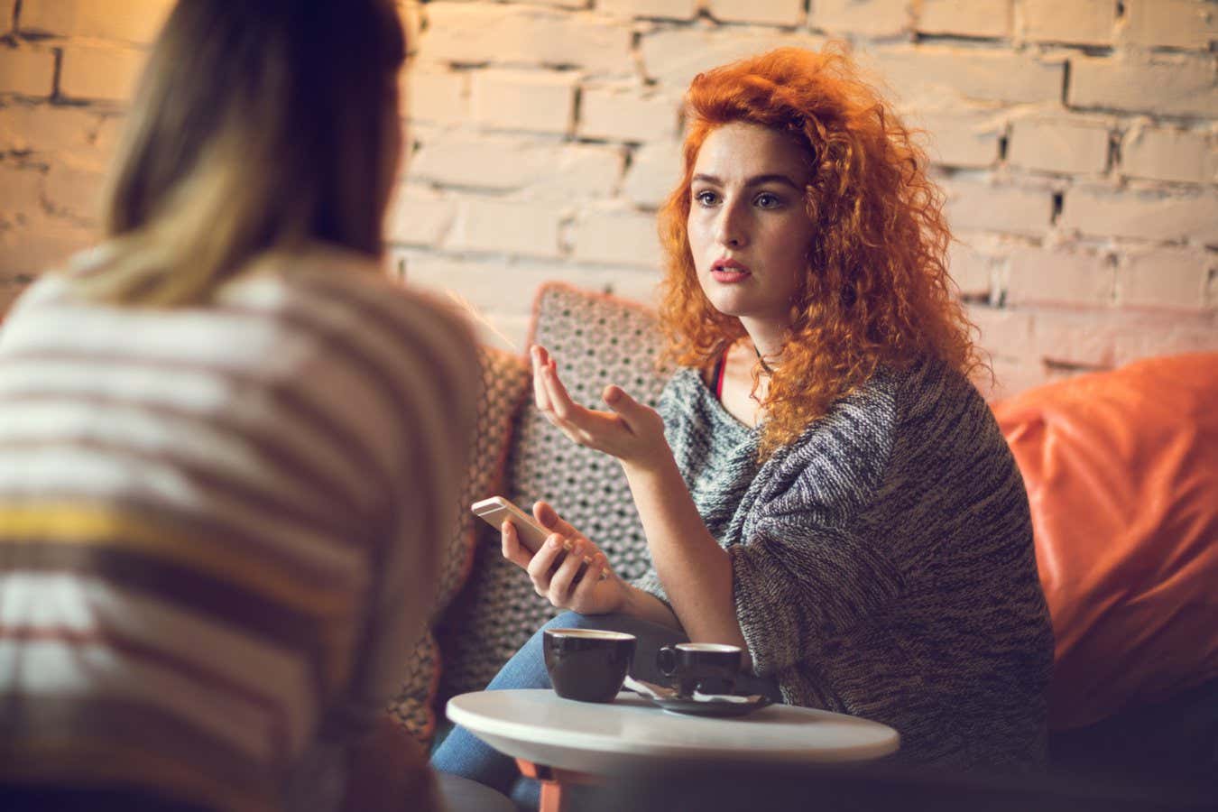 Young red-haired woman sitting in a cafe with friend and talking about something.