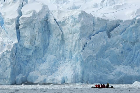 Tourists inspect a glacier from an inflatable Zodiac.