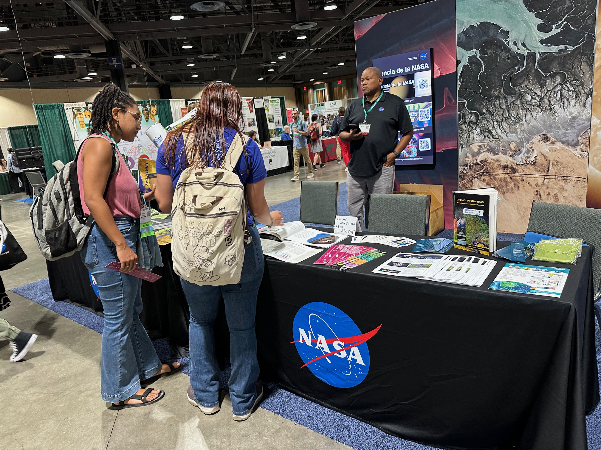 Two women page through Landsat materials at the NASA exhibit booth during the 2024 Ecological Society of America meeting.