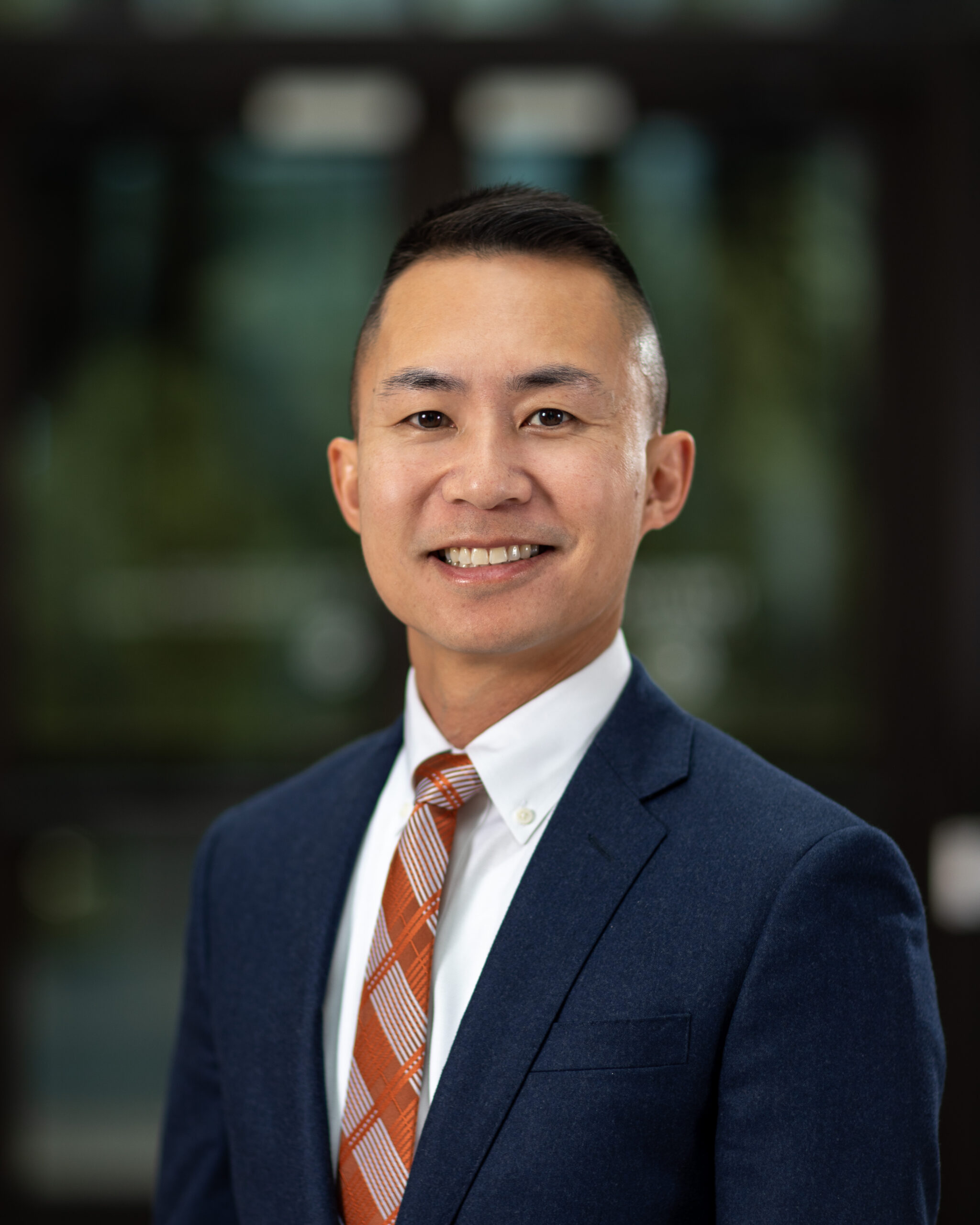 Portrait of Mathiew Le wearing an orange tie and blue suit jacket.