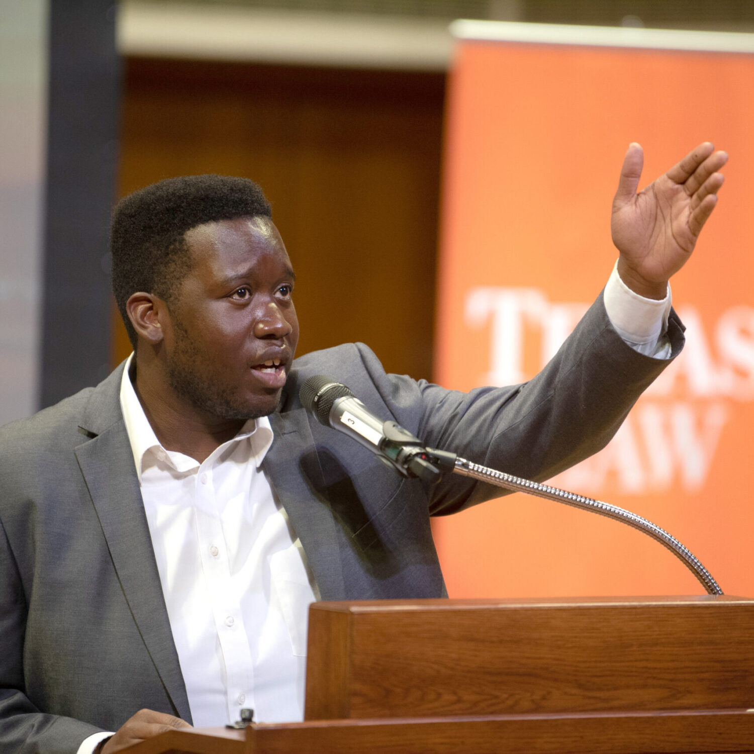 man with coat and white collared shirt speaking at a podium