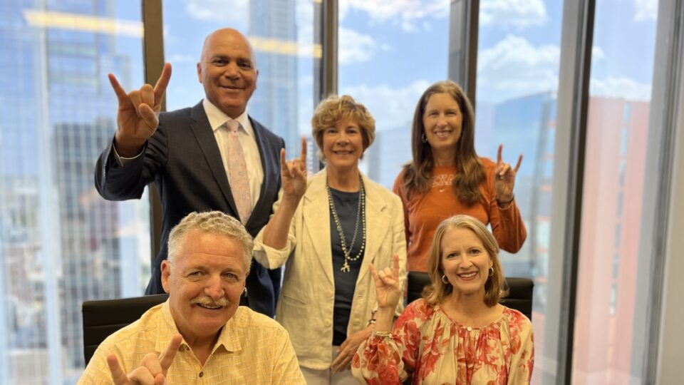 Five alumni pose with Hook Em signs