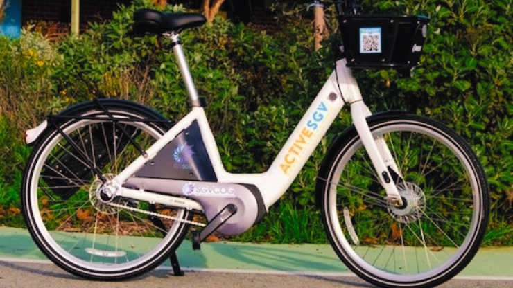 A white eBike parked in front of a bush