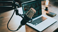 A microphone mounted on a stand near a laptop on a wooden desk.