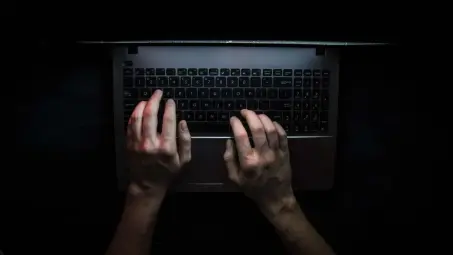 Hands typing on a laptop keyboard in a darkened room