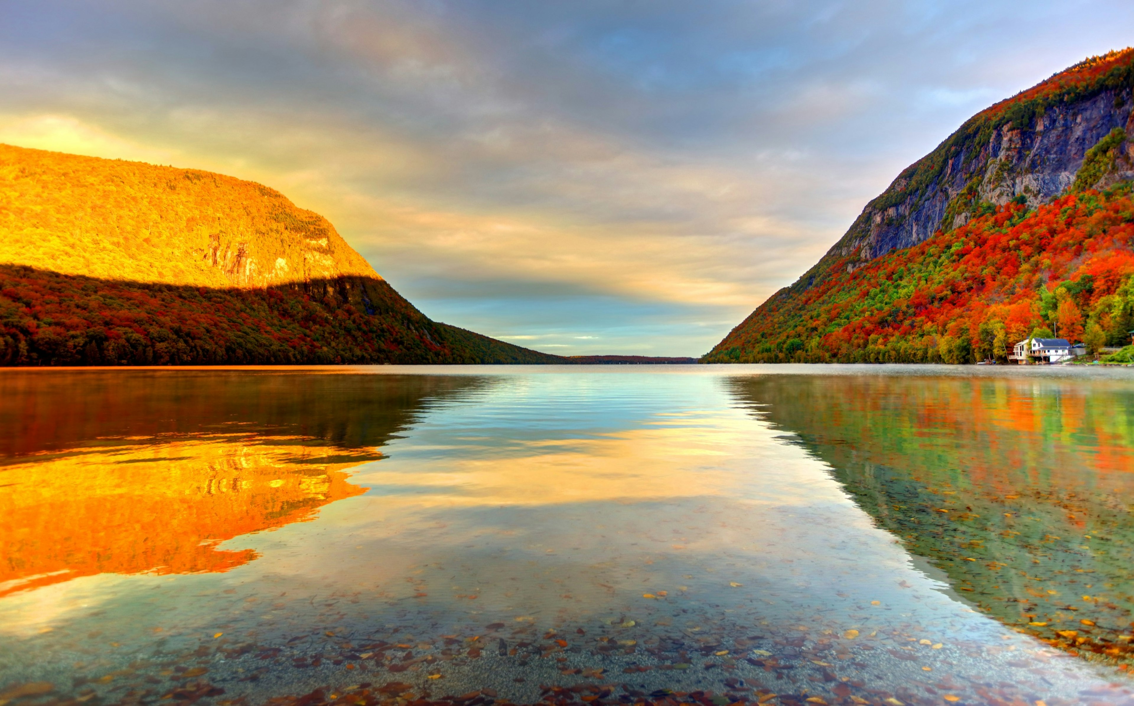 A lake at sunset reflects the yellow and red of the foliage on the surrounding hillsides