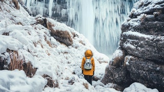 Woman with orange jacket standing below amazing frozen Pericnik waterfall .