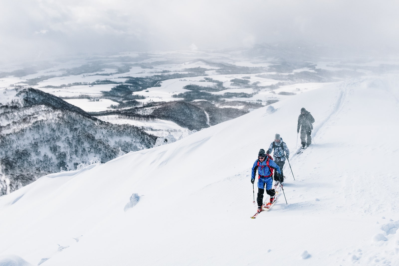 Three active tourists ski touring along the snowy mountain overlooking the beautiful valley in Japanese wilderness. Ski...