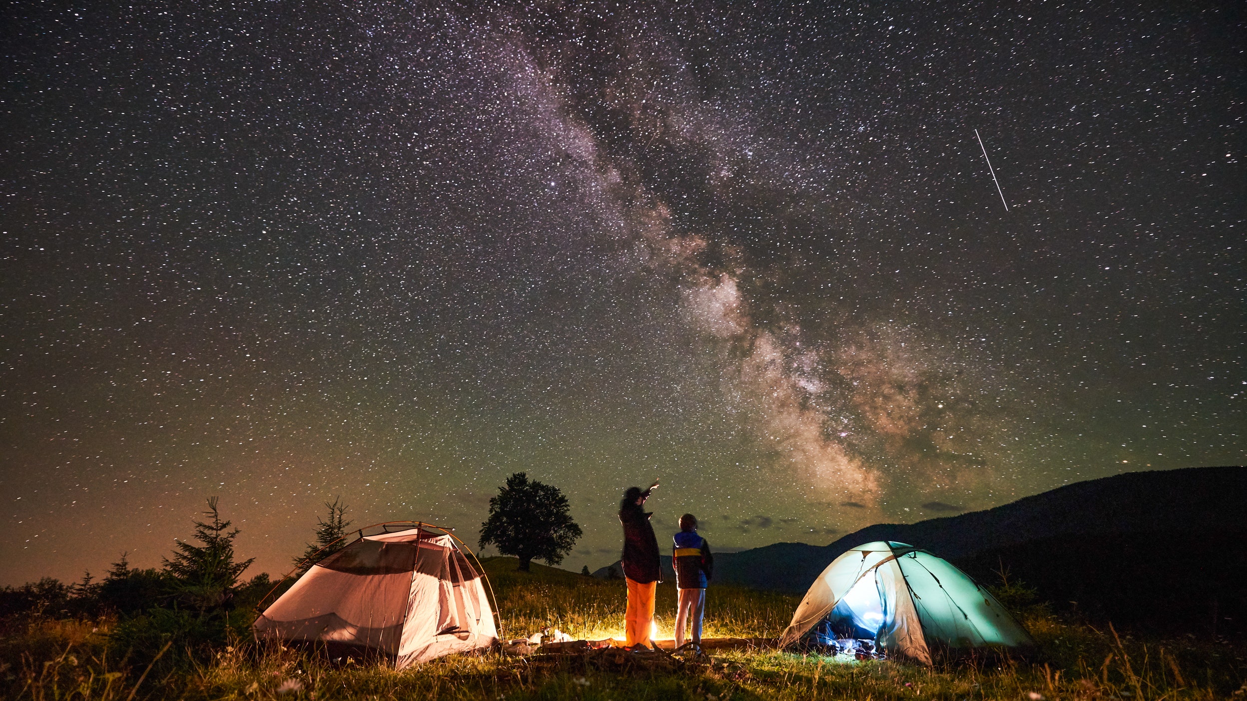 Mother and son camping in mountains below night sky full of stars