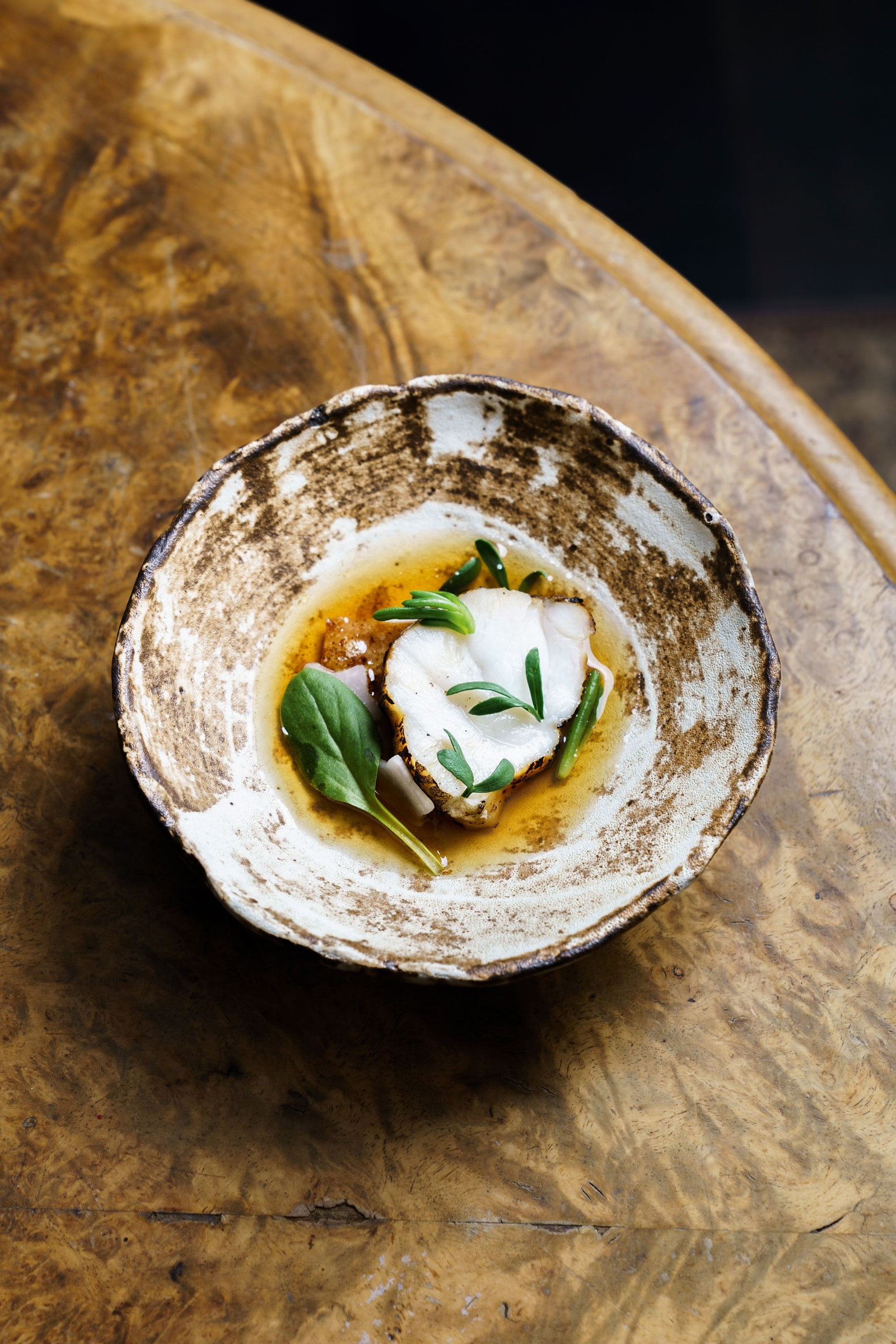 A round pottery dish containing white fish and green vegetables