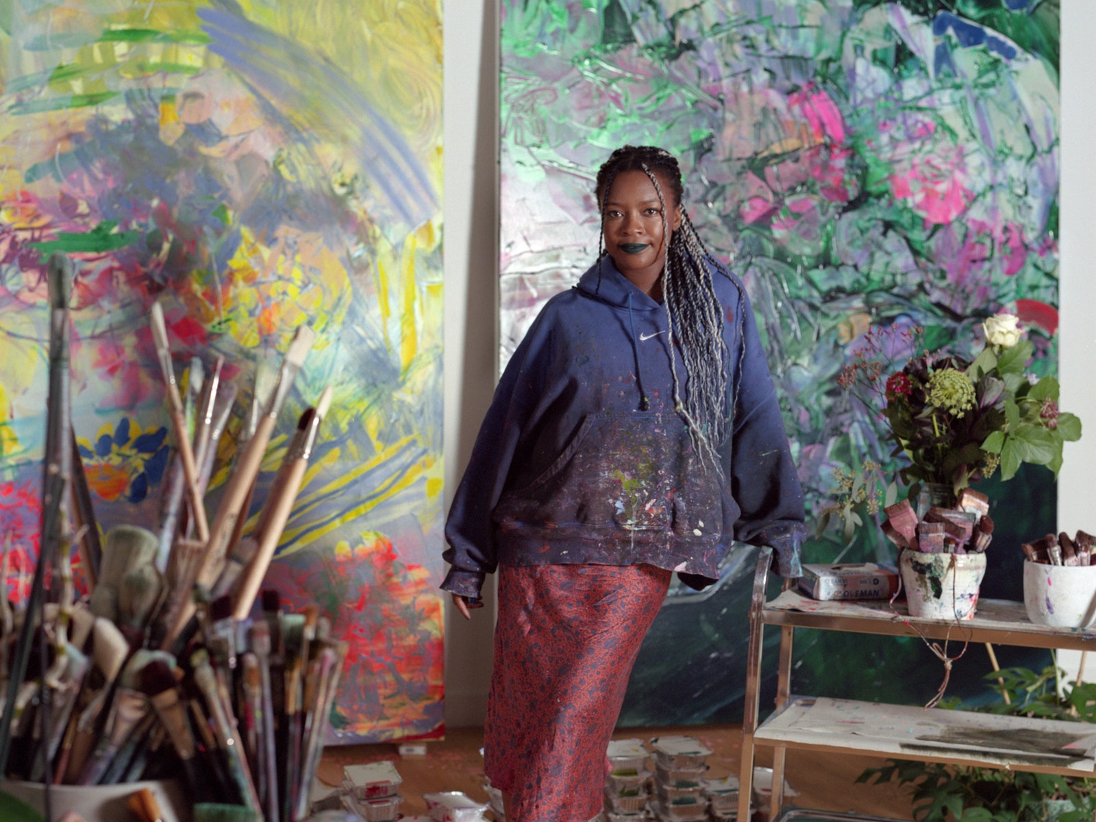 A photograph of the artist Jade Fadojutimi in front of two of her paintings