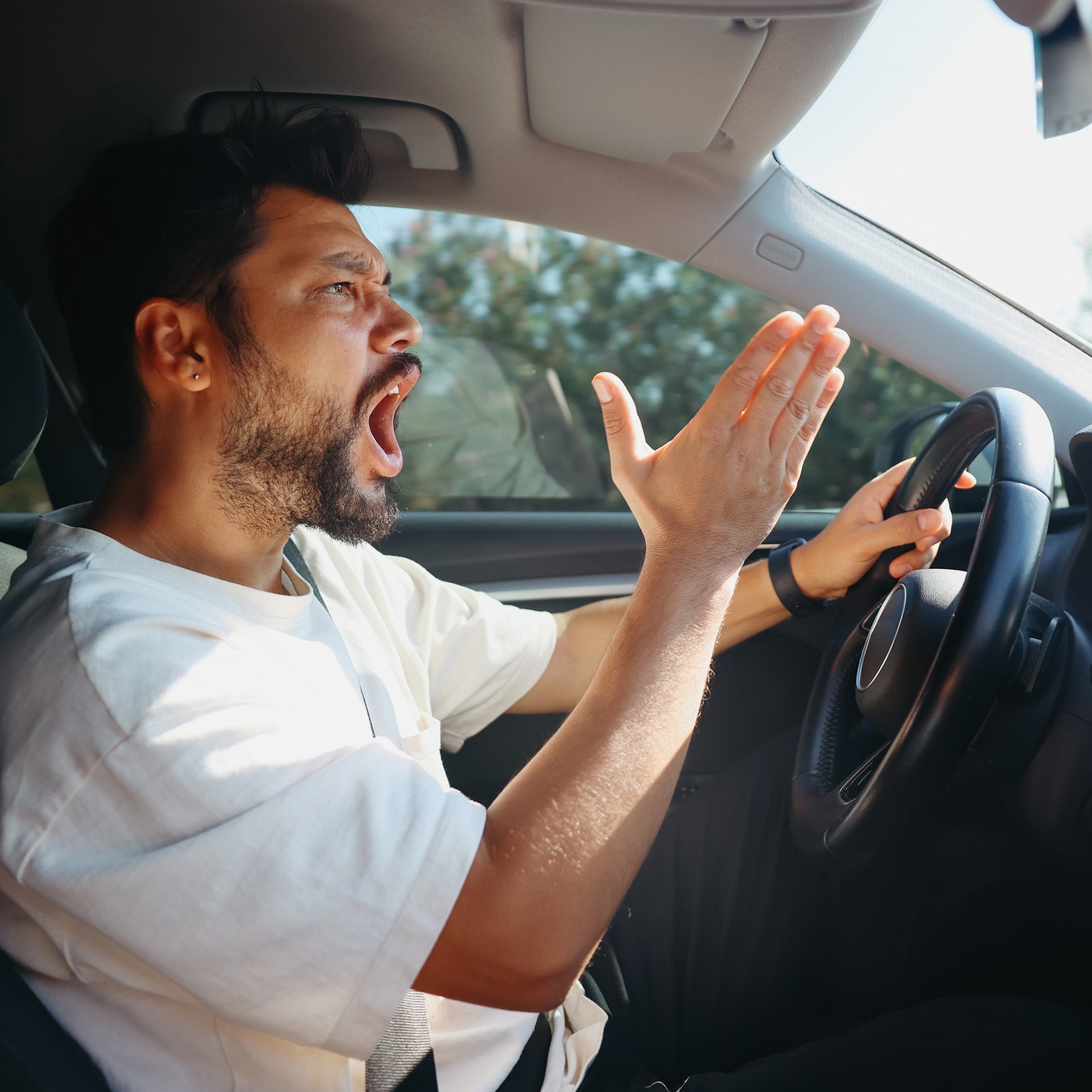 A man yells as he drives a car.