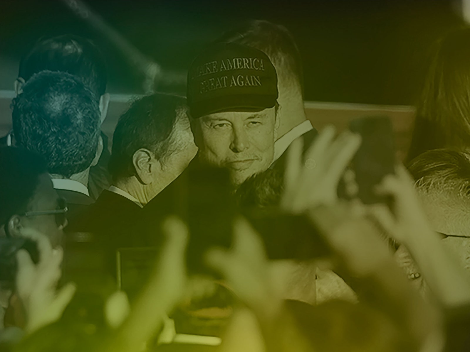 A photo of Elon Musk wearing a MAGA hat among a crowd.