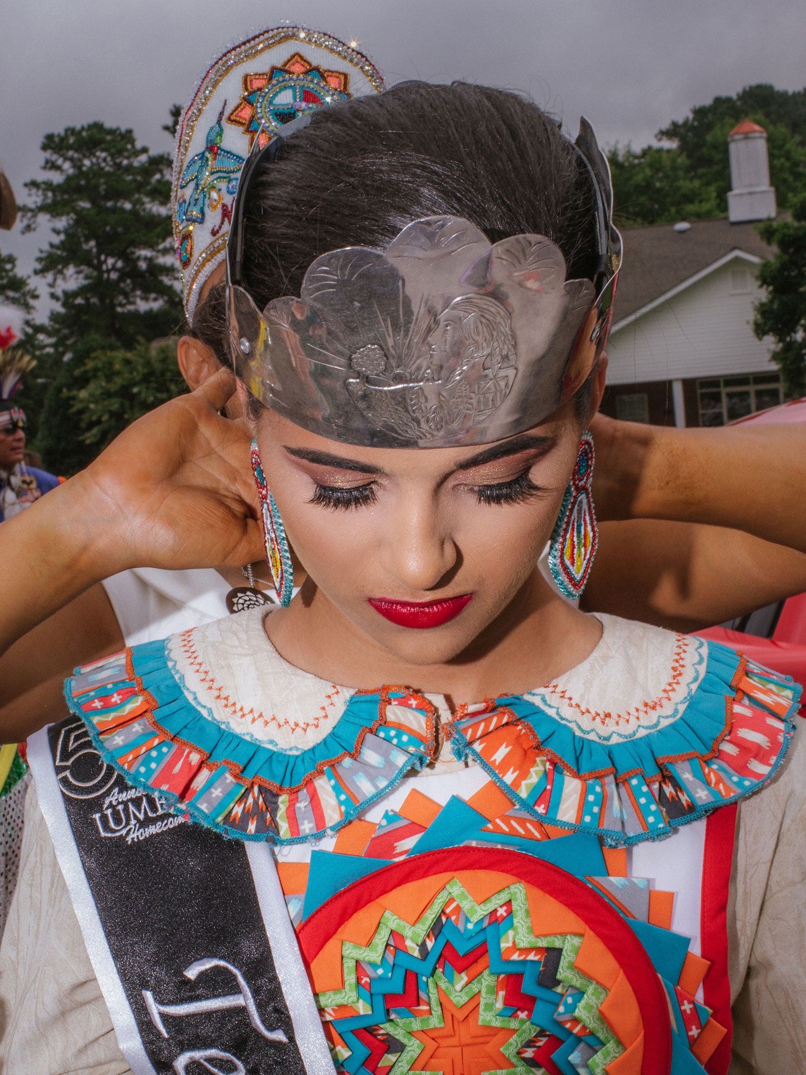 A woman looks down as hands adjust her pageant crown.