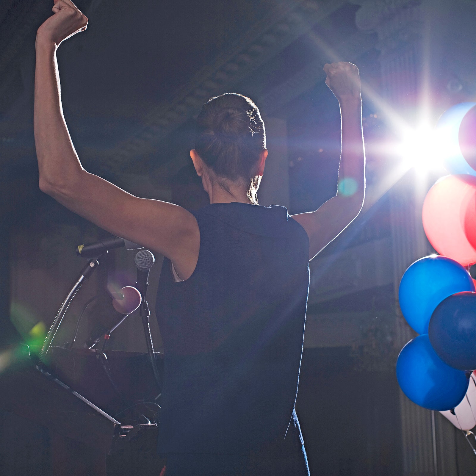 A person holds their arms up next to red white and blue balloons.