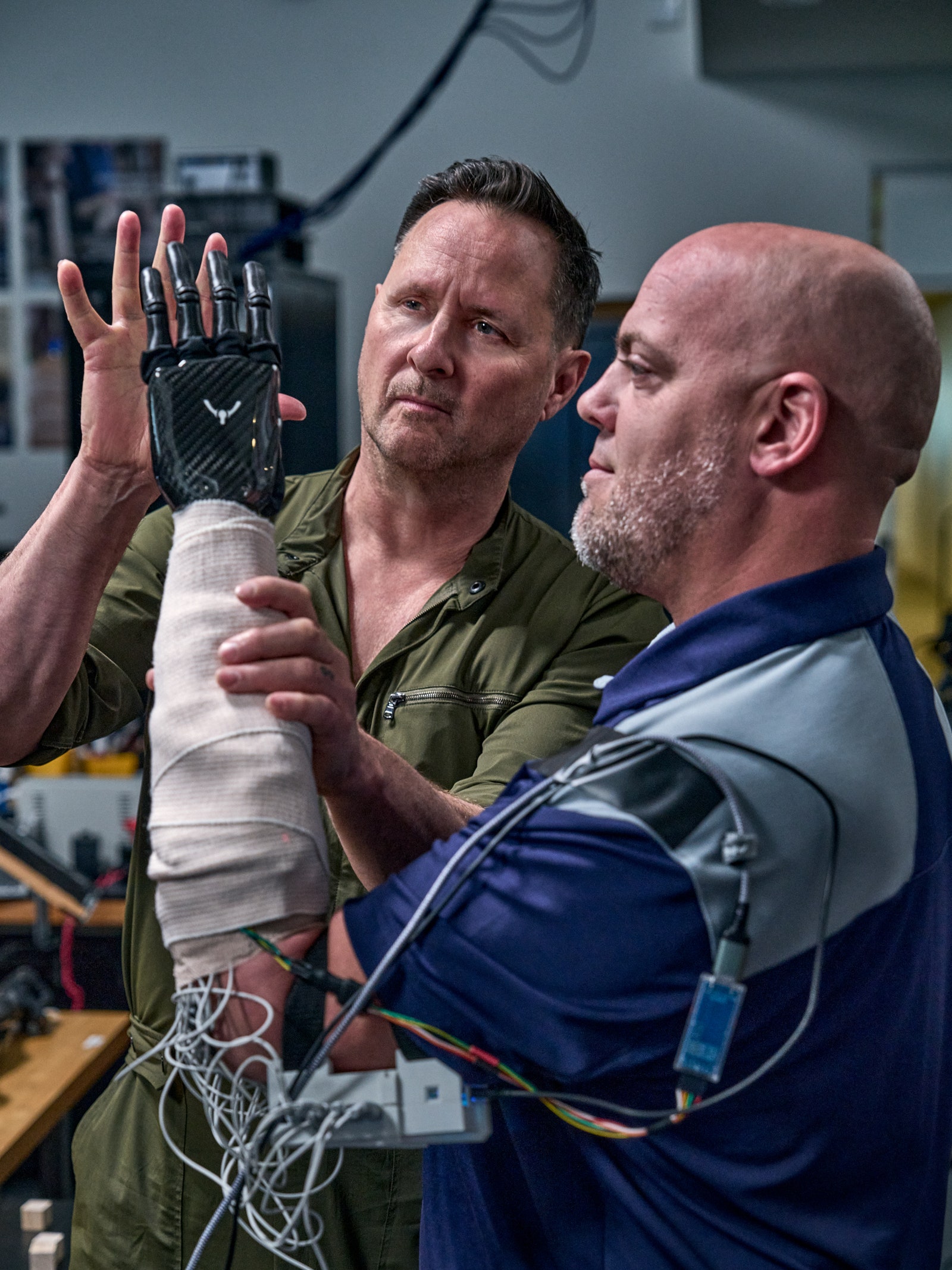 A person with a prosthetic arm that is wired up is reaching for the hand of another person.