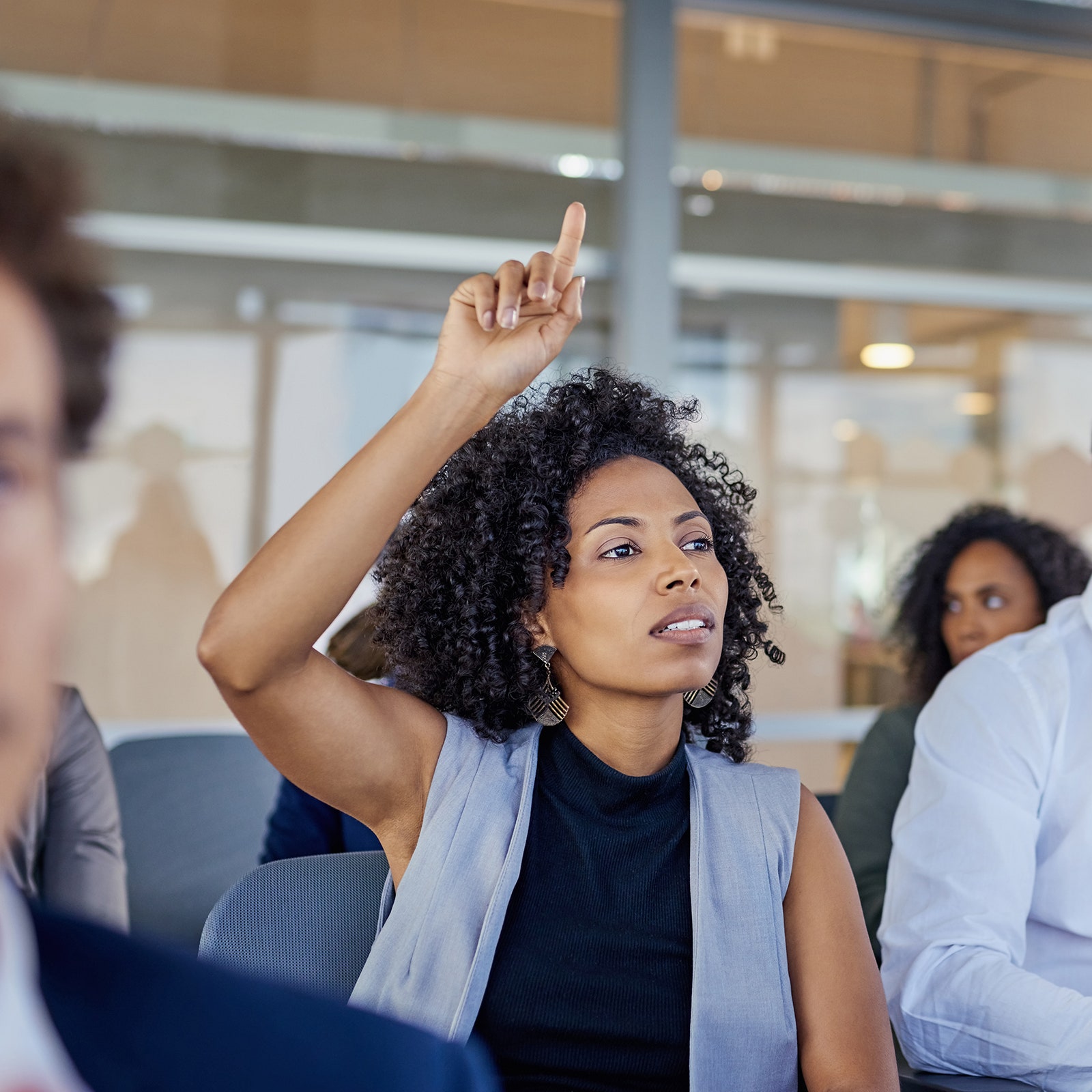 A photo of a person in an audience raising their hand to ask a question.