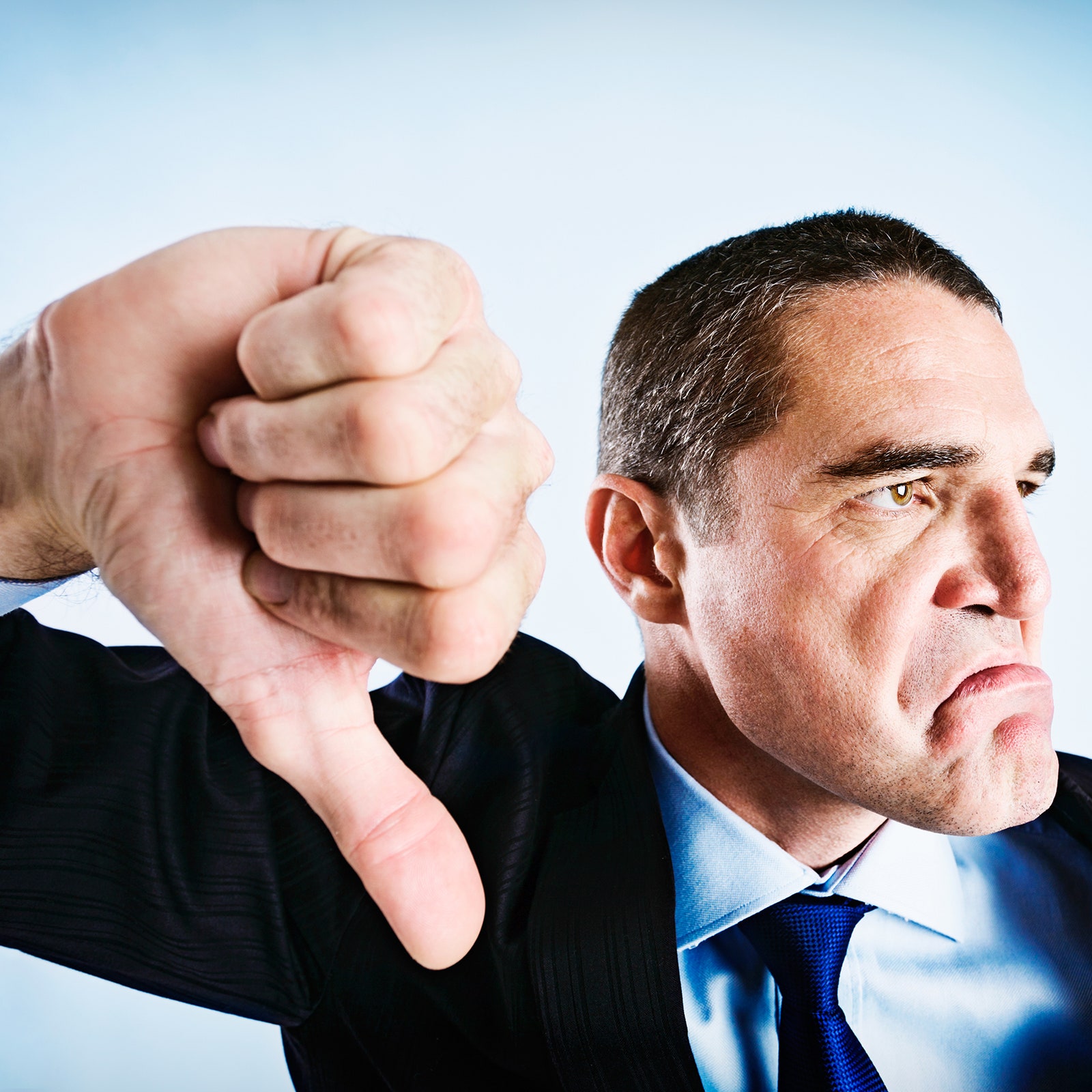 A photo of a man in a suit giving a thumbsdown signal.