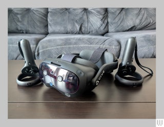 Front view of the HTC Vive Focus Vision a virtual reality headset and two handheld controllers all sitting on a dark...