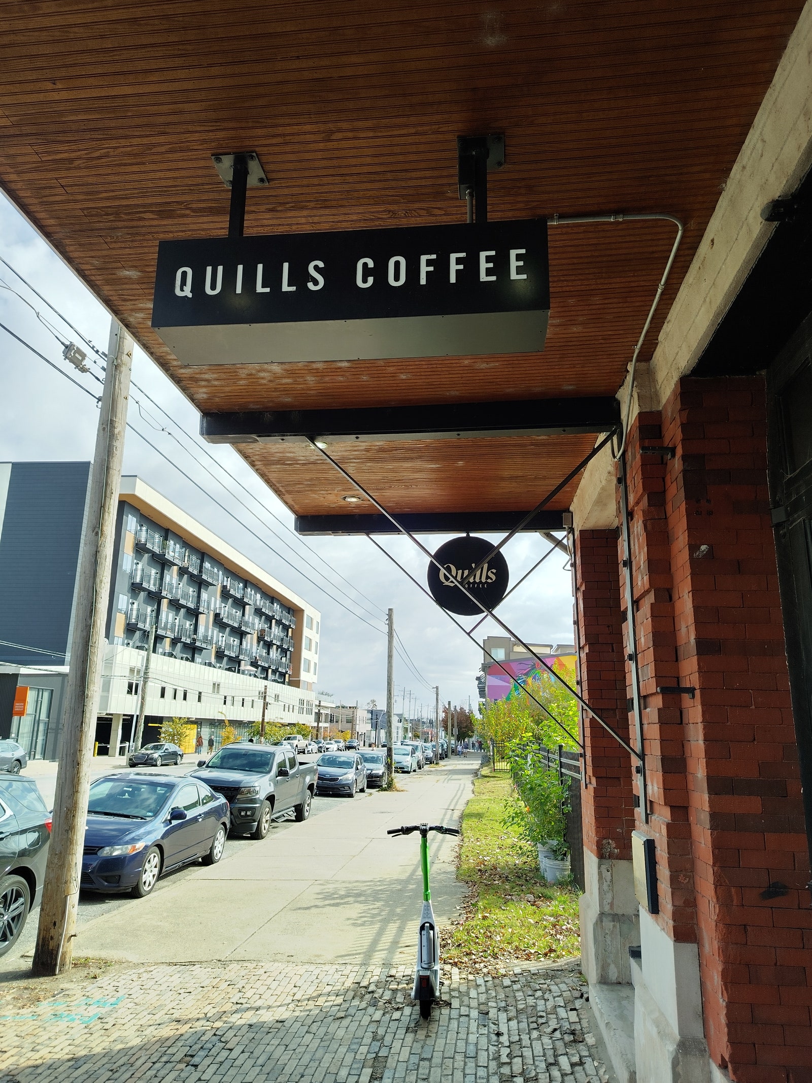 Upward view of hanging shop signs and parked cars along the sidewalk near the businesses