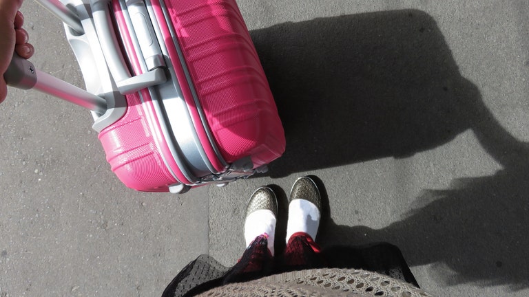 POV of a Woman with pink Carry on Luggage