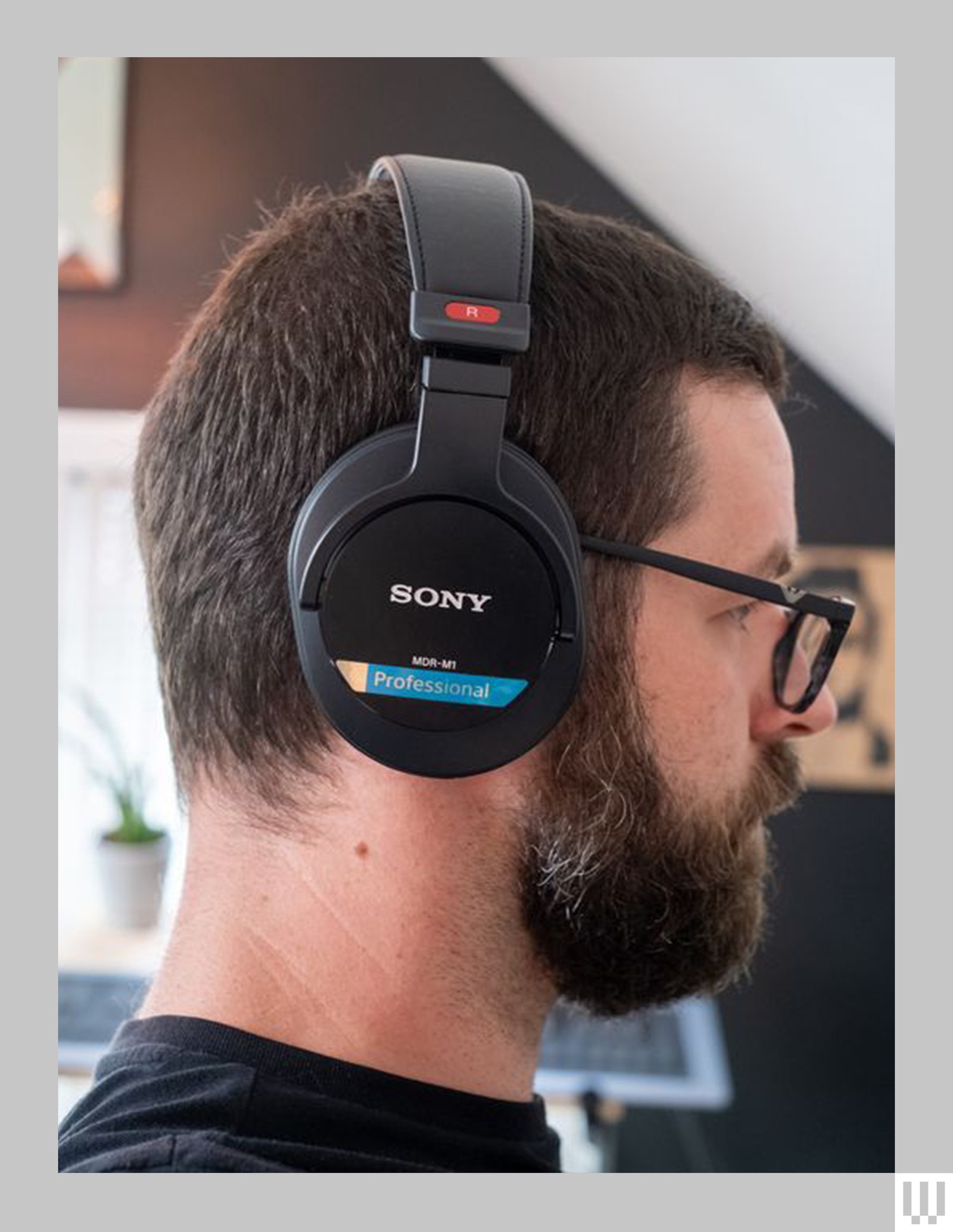 Side view of a person with dark hair a beard and glasses wearing Sony MDR M1 Studio Headphones black headphones with...