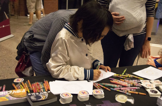 Child coloring a Psyche mission badge picture at a public event.