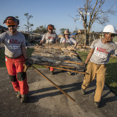 Four people carry debris away from a ruined home.