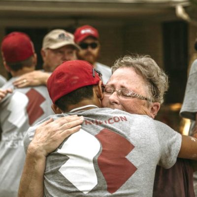 A young man wearing a Team Rubicon tshirt, hugs an older man.