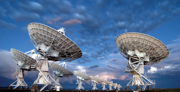 Photo of ten VLA antennas pointing at a cloudy sky at twilight.