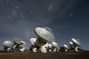 Photo of the moon-illuminated ALMA radio telescope array with stars in the background.