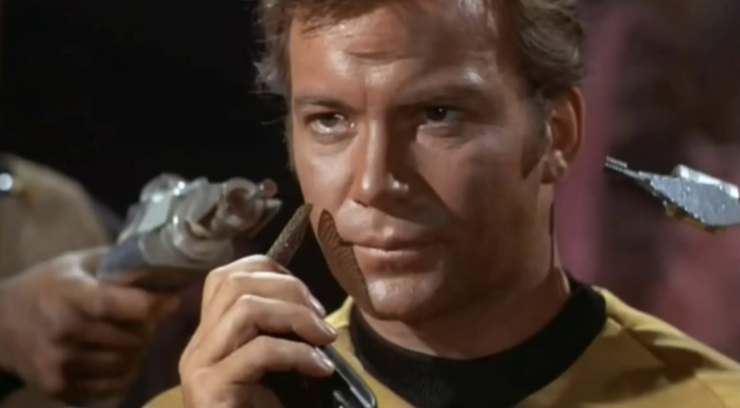 Kirk with phasers pointed at his head as he opens his communicator on Star Trek: TOS