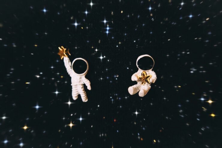 Image of two astronaut figurines holding gold stars, floating against a field of distant stars