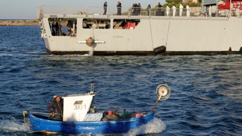 A fishing boat motors past a navy boat carrying migrants intercepted in Italian waters arriving at Shengjin port in Albania on October 16, 2024.